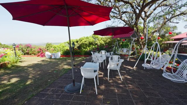 Outdoor garden cafe with red umbrellas white chairs and lush greenery under a clear blue sky