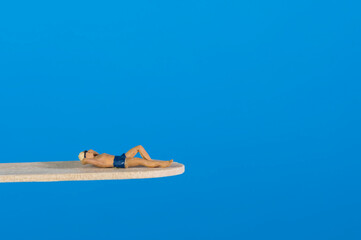 Swimmer relaxes on a diving board, blue background