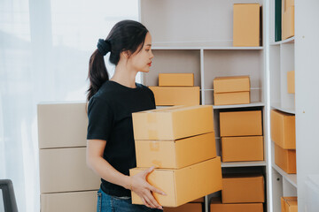 Asian small business owner working in home office with boxes, checking orders and preparing for...