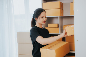 Fototapeta na wymiar Asian small business owner working in home office with boxes, checking orders and preparing for delivery to customers. Online Marketing, SME Ecommerce Concepts