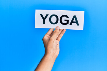 Hand of caucasian man holding paper with yoga word over isolated blue background