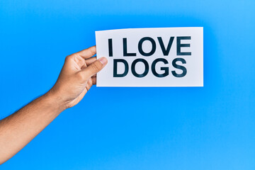 Hand of caucasian man holding paper with i love dogs message over isolated blue background