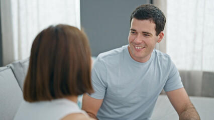 Beautiful couple sitting on sofa looking each other smiling at home