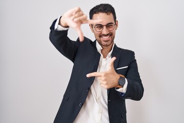 Handsome business hispanic man standing over white background smiling making frame with hands and fingers with happy face. creativity and photography concept.