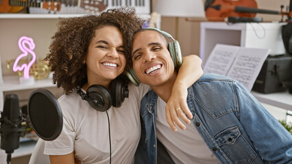 Smiling musicians at music studio, wearing headphones and hugging each other while confidently playing song