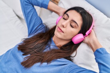 Young beautiful hispanic woman listening to music lying on bed at bedroom