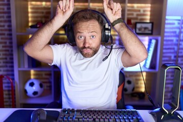 Middle age man with beard playing video games wearing headphones doing funny gesture with finger...
