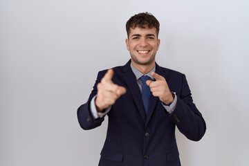 Young hispanic business man wearing suit and tie pointing fingers to camera with happy and funny face. good energy and vibes.