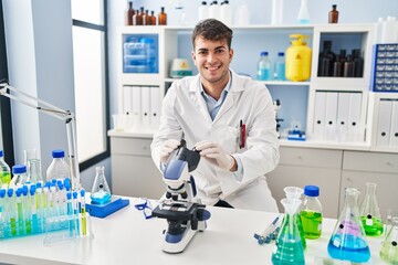 Young hispanic man scientist smiling confident using microscope at laboratory