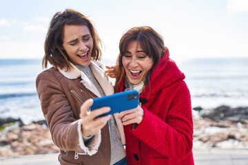 Two women mother and daughter using smartphone at seaside