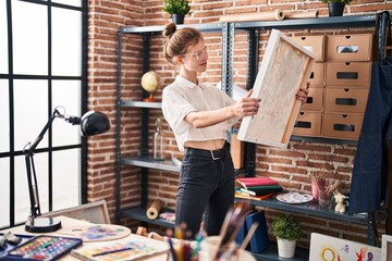 Blonde woman examines artwork in a creative studio interior, surrounded by painting supplies and...