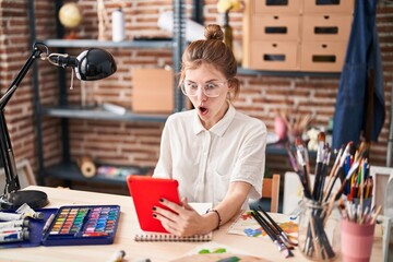 Stunned young blonde artist woman, open-mouthed in shock and disbelief, looking at tablet screen in...