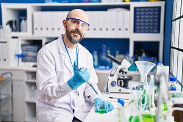 Young bald man scientist pouring liquid on test tube at laboratory