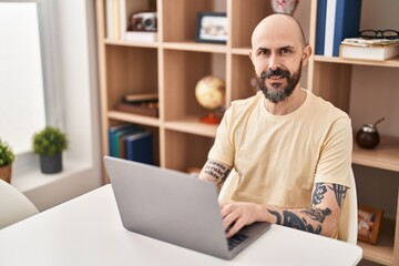 Young bald man using laptop sitting on table at home