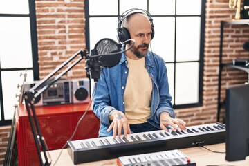 Young bald man musician playing piano at music studio