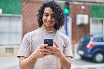 Fototapeta na wymiar Young latin man smiling confident using smartphone at street