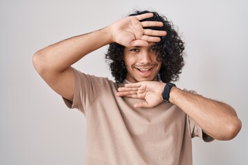 Hispanic man with curly hair standing over white background smiling cheerful playing peek a boo with hands showing face. surprised and exited