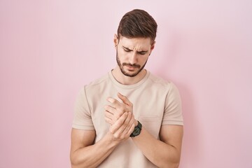 Hispanic man with beard standing over pink background suffering pain on hands and fingers,...