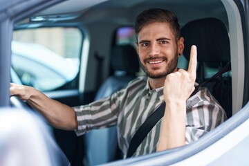 Hispanic man with beard driving car smiling with an idea or question pointing finger with happy face, number one