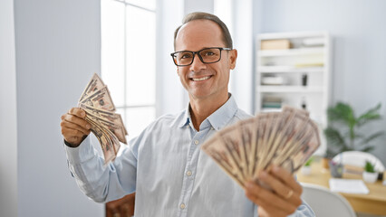Smiling middle age man confidently handling dollars in his office, a happy worker showcasing...