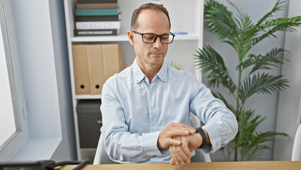 Middle age man business worker looking watch sitting on table at the office