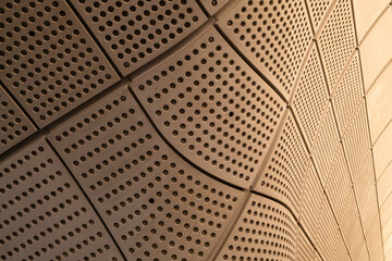 Curved and perforated contemporary wall panels bend around a structure in warm colours. Looks like...