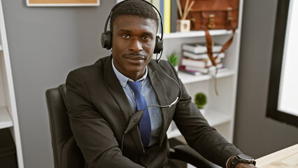 Handsome african man wearing a headset and suit seated in a modern office.