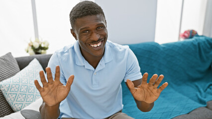 Smiling african american man casually dressed in a living room with sofa and decorative pillows.