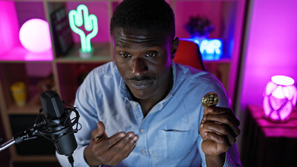 African man holding bitcoin with microphone in a colorful, illuminated gaming room at night