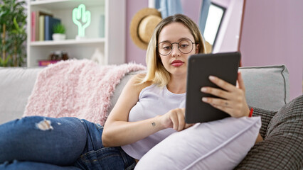 Obraz premium Young blonde woman using touchpad sitting on sofa at home