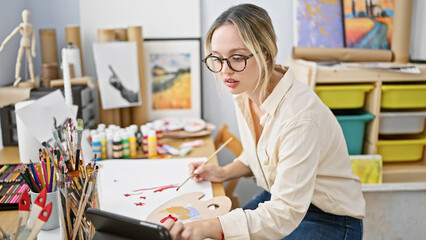 Young blonde woman artist drawing on paper using touchpad at art studio
