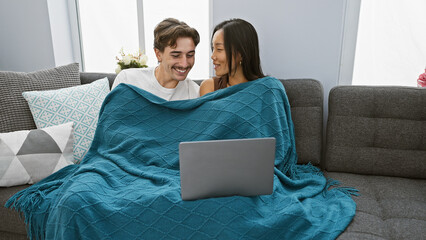 Interracial couple enjoying time together with laptop in cozy living room.