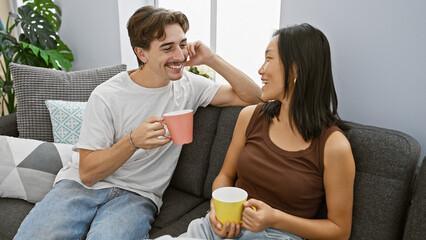Interracial couple enjoying coffee together on a cozy sofa in a modern apartment living room.