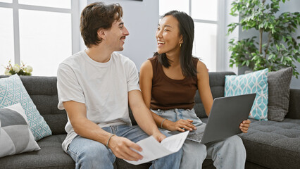 Interracial couple happily sharing documents in a modern living room, depicting a man and woman together indoors.