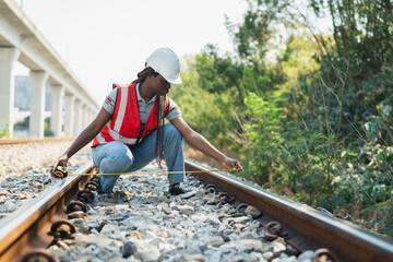 African American female railway engineer in vest and helmet safety inspecting and checking railroad tracks by using measuring tape to measure railroad tracks length