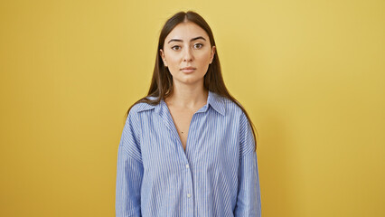 Portrait of a young hispanic woman standing confidently against a yellow wall, exuding beauty and...