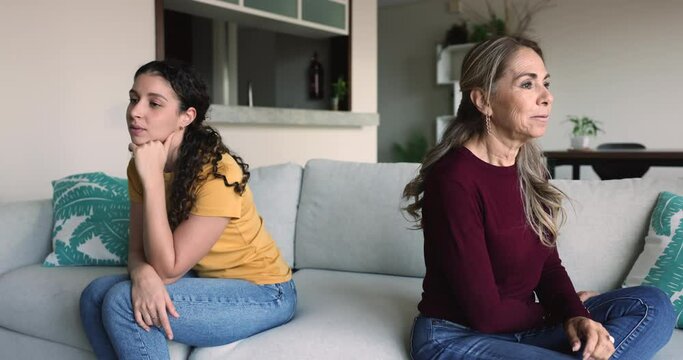 Upset mom and daughter sit on sofa separately expressing dissatisfaction after quarrel, opinions differ, lack of understanding, difficult teen age, go through relation problems due to generational gap