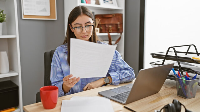 Focused young hispanic woman reviewing a document in an office setting.