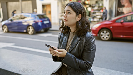 Fototapeta premium Young hispanic woman using smartphone on a vibrant city street