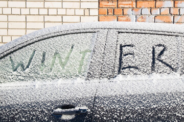 The word WINTER is painted on the glass of a car made of snow. The concept.