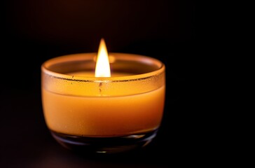 Close-up of a burning candle in a glass holder, against a dark background