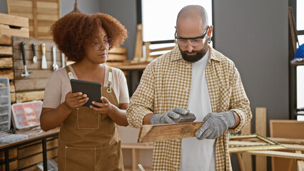 Two expert carpenters in the throes of sanding a wood plank using touchpad, embracing technology in...