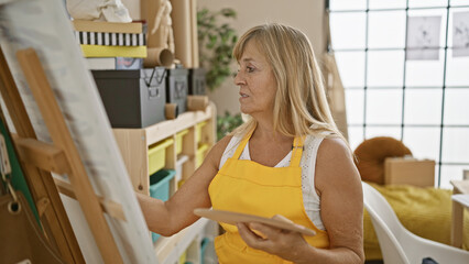 Serious and relaxed, middle age blonde woman artist passionately draws in the art studio, fully...