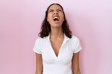 Fototapeta premium Young hispanic woman wearing casual white t shirt angry and mad screaming frustrated and furious, shouting with anger. rage and aggressive concept.