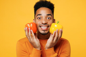 Close up happy young man wear orange sweatshirt casual clothes hold in hand many bell peppers near...