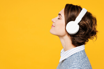 Side view close up young woman wears grey knitted sweater shirt casual clothes listen to music in headphones close eyes raise up hands isolated on plain yellow background studio. Lifestyle concept.