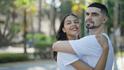Fototapeta premium Confident, beautiful couple hugging and joyfully smiling in a sunny park, expressing love and happiness while enjoying a casual, outdoor lifestyle.