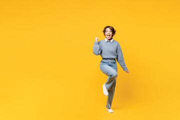 Full body young woman she wears grey knitted sweater shirt casual clothes doing winner gesture celebrate clenching fists say yes isolated on plain yellow background studio portrait. Lifestyle concept. - obrazy, fototapety, plakaty