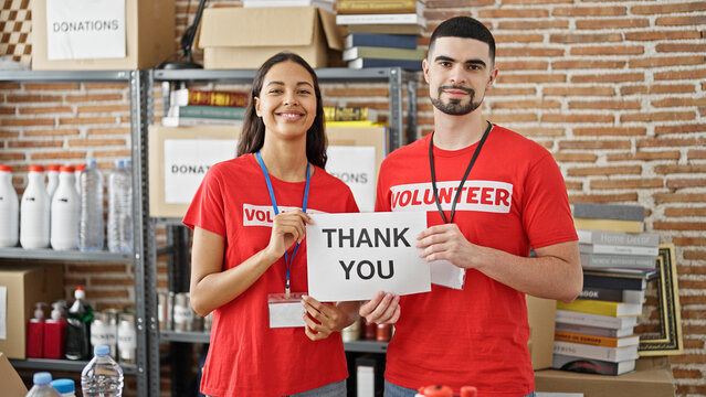 Confident young man and woman volunteers, standing in unity at charity center, holding a heartfelt 'thank you' paper banner in spotlight of altruism.