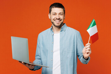 Young IT man he wears blue shirt white t-shirt casual clothes hold Italian flag use work on laptop...